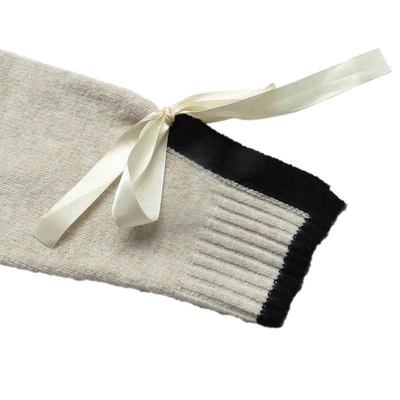 A close-up of a cream-colored knit sleeve with a black ribbed cuff and a cream satin ribbon tied in a bow, set against a plain white background.