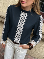 A woman wearing a navy blue long-sleeve blouse with white lace trim down the front and along the sleeves, paired with white pants.
