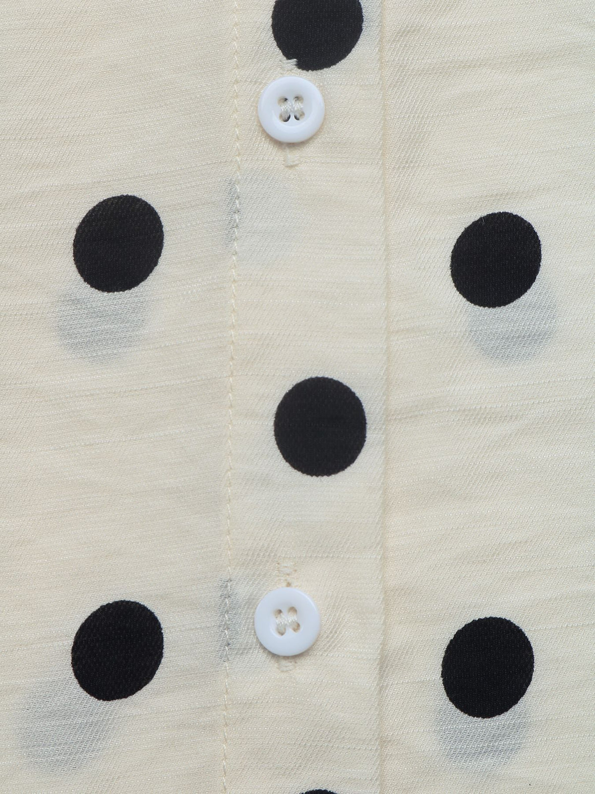 Close-up of a cream-colored fabric with black polka dots and white buttons on a button-up shirt.