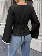 A woman shown from the back wearing a black long-sleeve top with a lace-up waist tie and white lace trim at the cuffs, paired with light blue jeans.