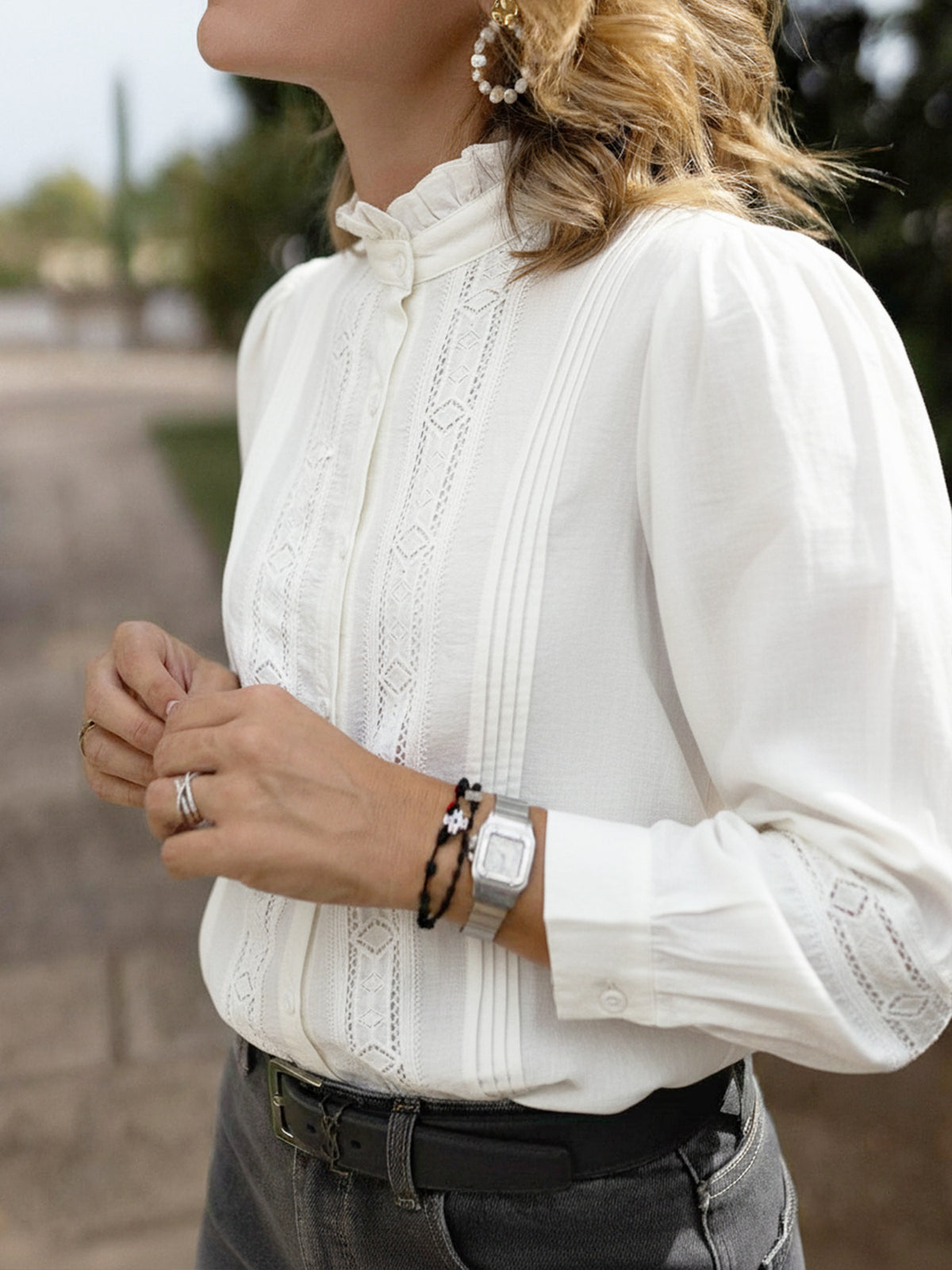 Person wearing a white blouse with lace details, black pants, and accessories.