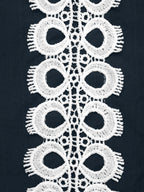 White lace trim with a repeating scalloped eyelet pattern, shown laid flat against a dark navy fabric background.