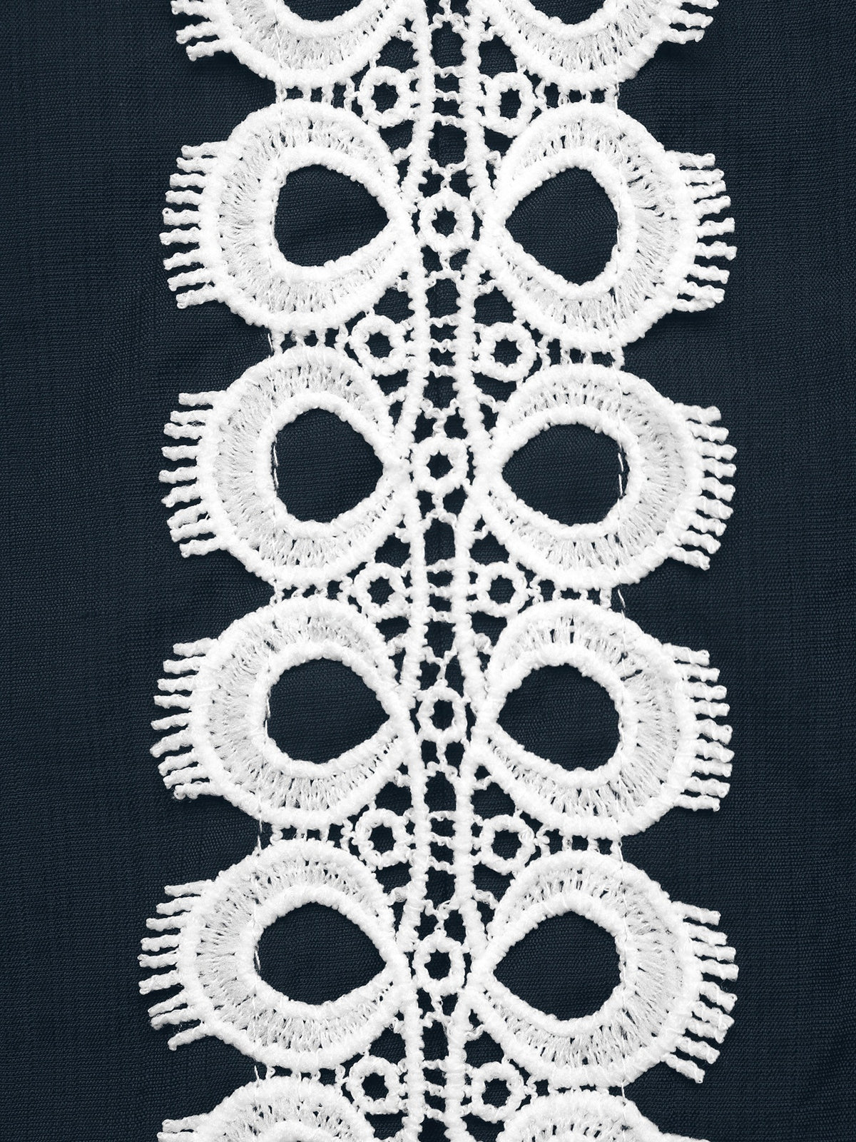 White lace trim with a repeating scalloped eyelet pattern, shown laid flat against a dark navy fabric background.