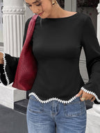 A woman wearing a black long-sleeve top with white leaf-trimmed cuffs and hem, paired with blue jeans and carrying a burgundy quilted shoulder bag.
