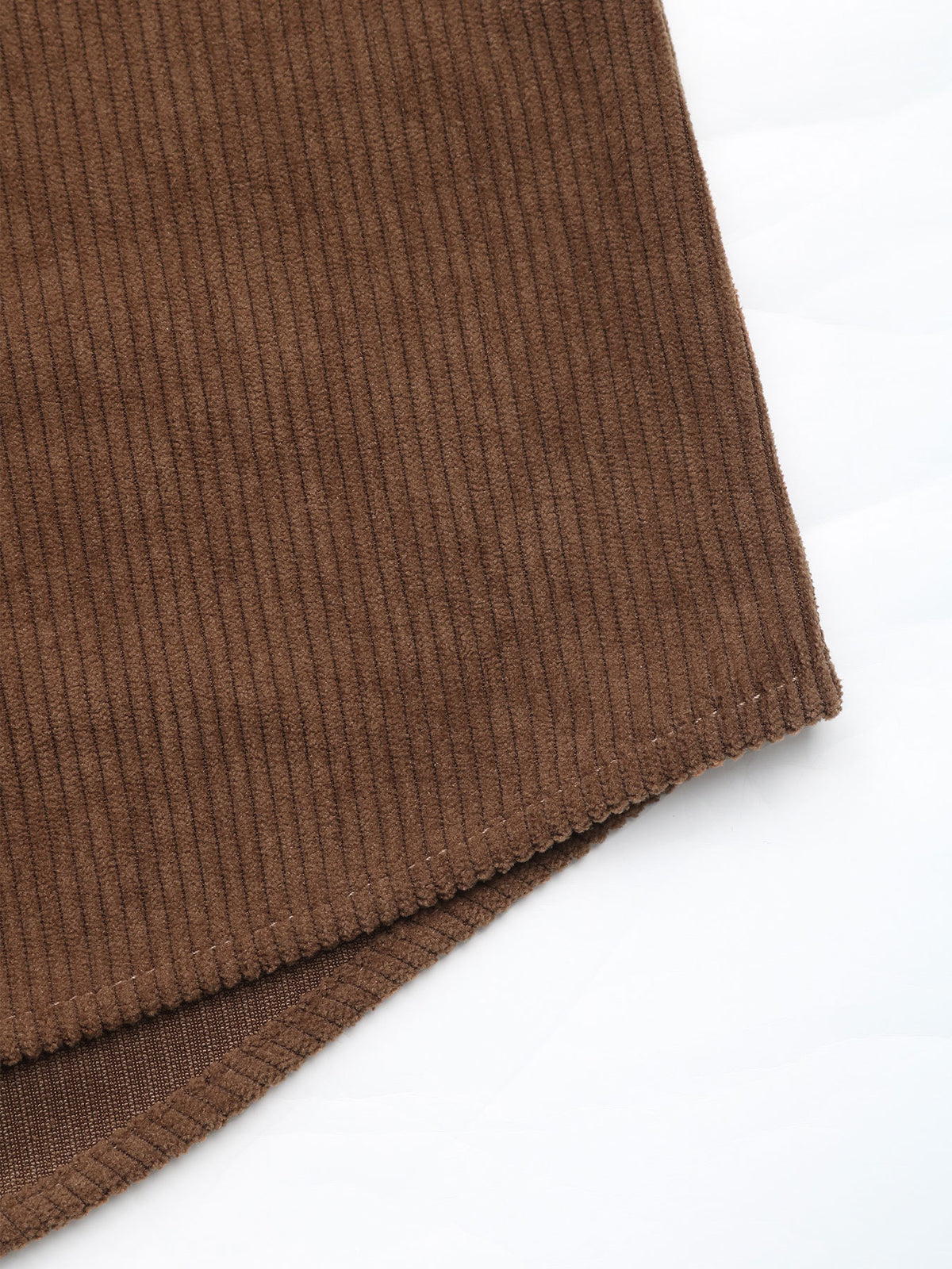 Close-up of a brown ribbed corduroy fabric corner with a stitched hem, laid on a white background.
