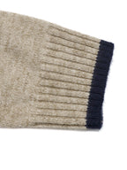 Close-up of a ribbed knit sweater cuff in a heathered oatmeal beige color with a contrasting dark navy blue ribbed trim, shown on a plain white background.