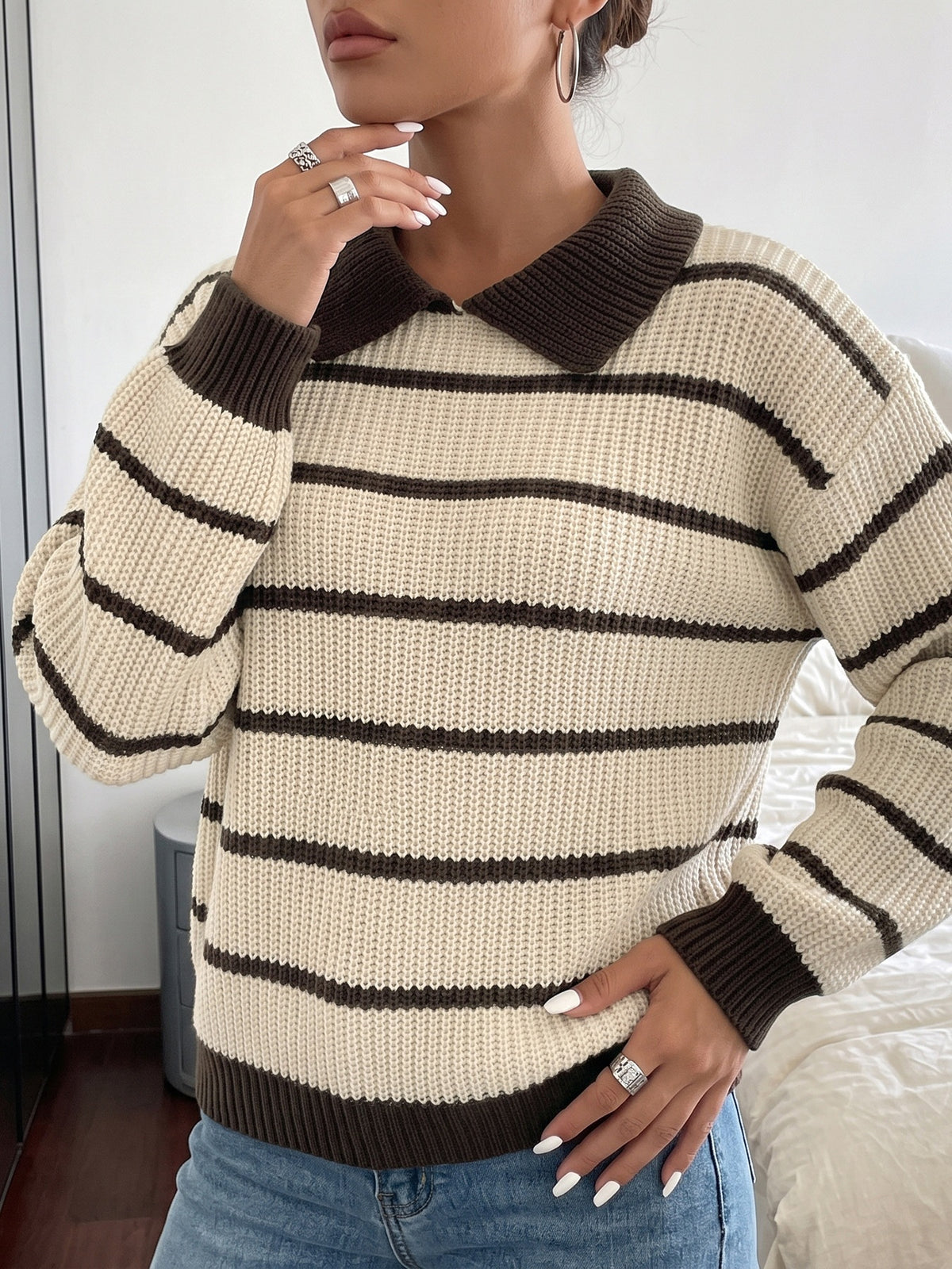 A woman wearing a cream and dark brown horizontally striped knit sweater with a dark brown collar, cuffs, and hem, paired with blue jeans.