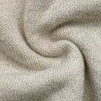 A close-up of soft knit fabric in a warm off-white or cream tone, arranged in a gentle spiral to show texture and drape.
