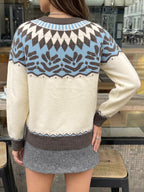 A woman wearing a cream, brown, and light blue Fair Isle knit sweater, shown from the back in a cafe setting.