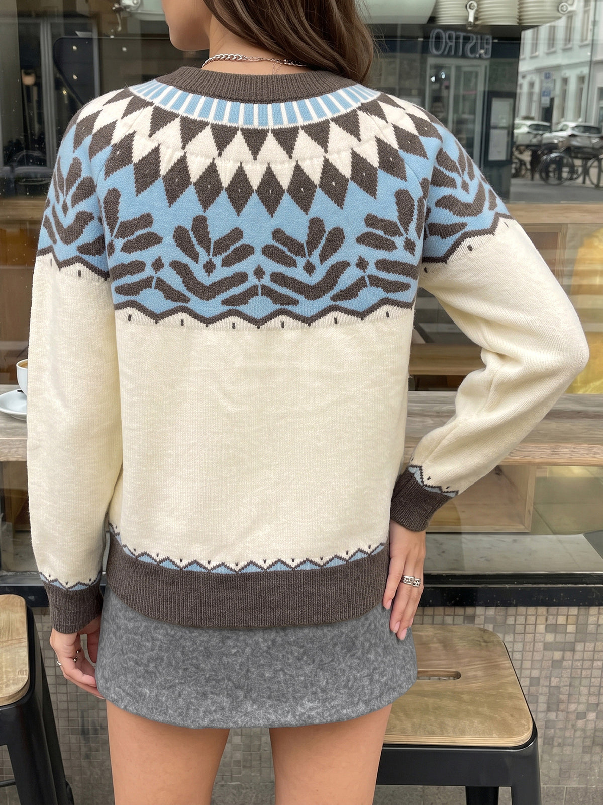 A woman wearing a cream, brown, and light blue Fair Isle knit sweater, shown from the back in a cafe setting.