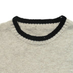 Close-up of a knit sweater showing a light beige body with a contrasting black ribbed crew neck trim.