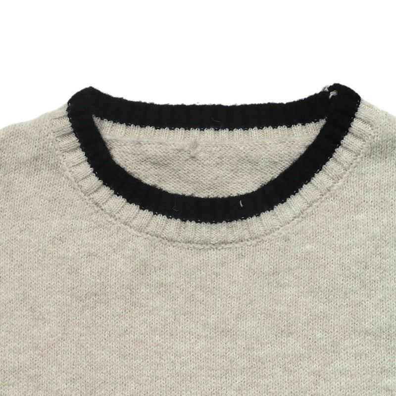 Close-up of a knit sweater showing a light beige body with a contrasting black ribbed crew neck trim.