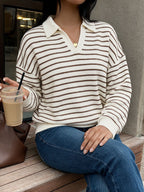 A woman wearing a cream and brown horizontally striped knit polo sweater sits on a wooden bench, holding an iced coffee.