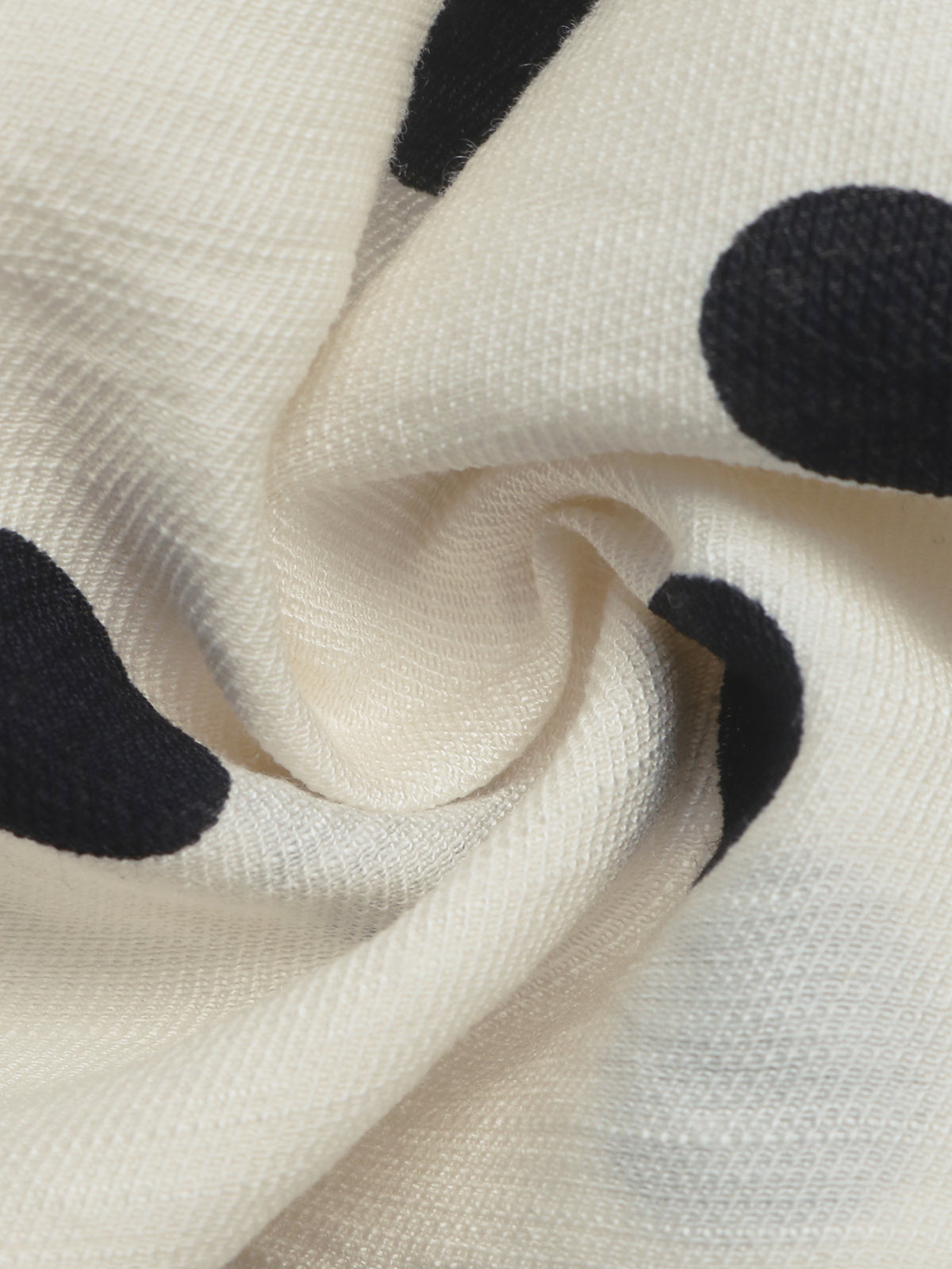 Close-up of a cream-colored knit fabric with large black polka dots, shown in a swirled drape to highlight the texture and pattern.