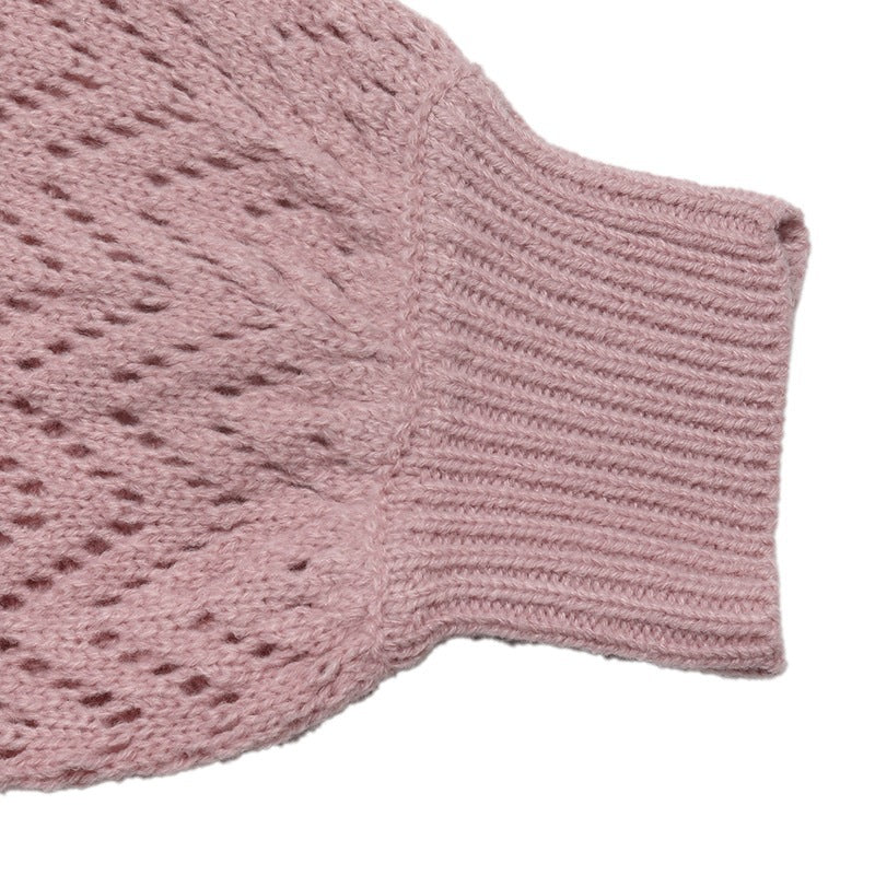 Close-up of a dusty pink knit garment showing a textured openwork pattern and a ribbed cuff on a white background.