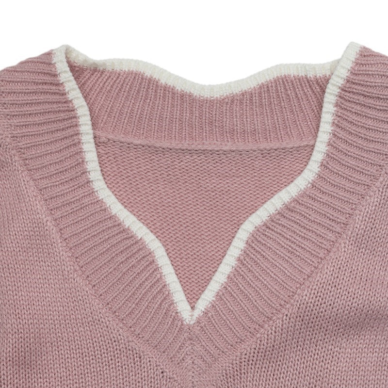 Close-up of a pink knit V-neck sweater with a contrasting white ribbed trim along the neckline.