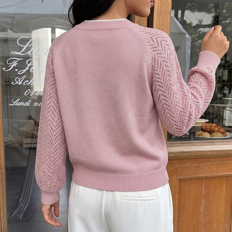 A woman wearing a light pink knit sweater with textured openwork sleeves, shown from the back in a cafe setting.