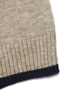 Close-up of a ribbed knit garment corner showing a heathered beige body with a dark navy ribbed cuff on a white background.