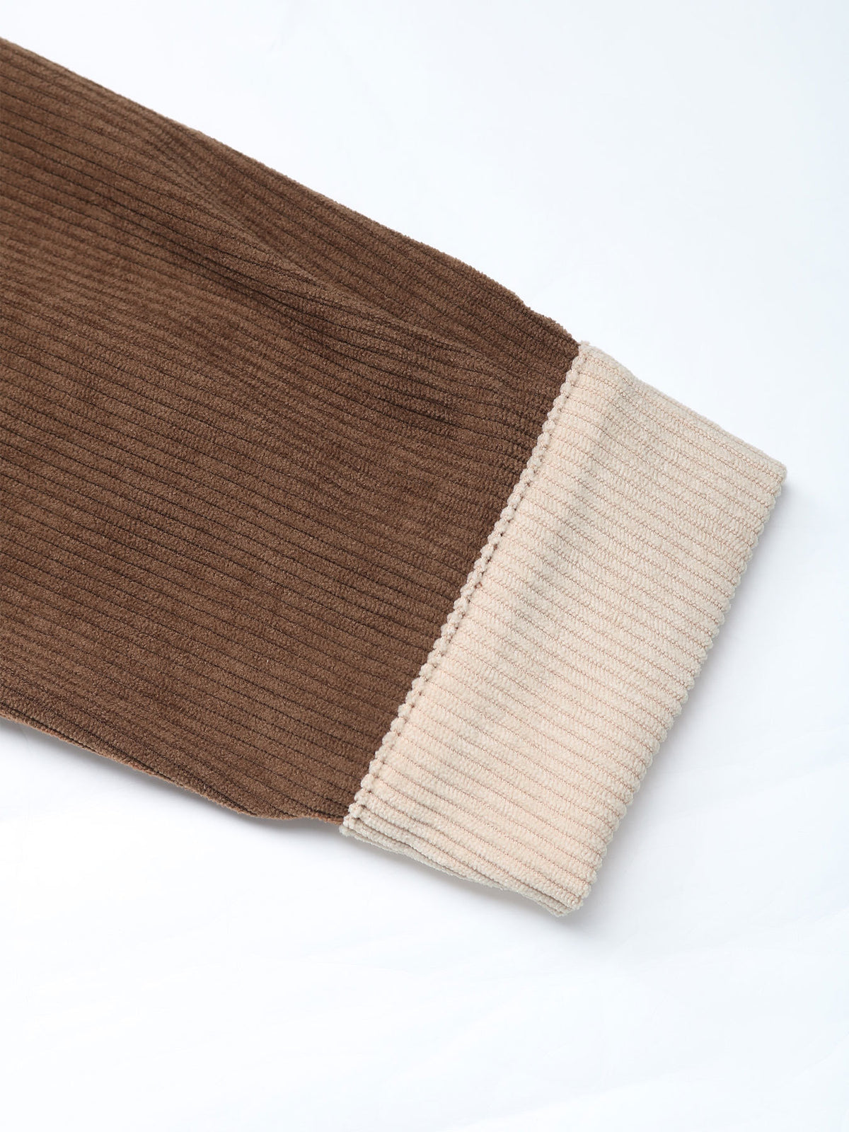 A close-up of a ribbed knit garment sleeve showing a dark brown main body and a contrasting light beige cuff on a white background.