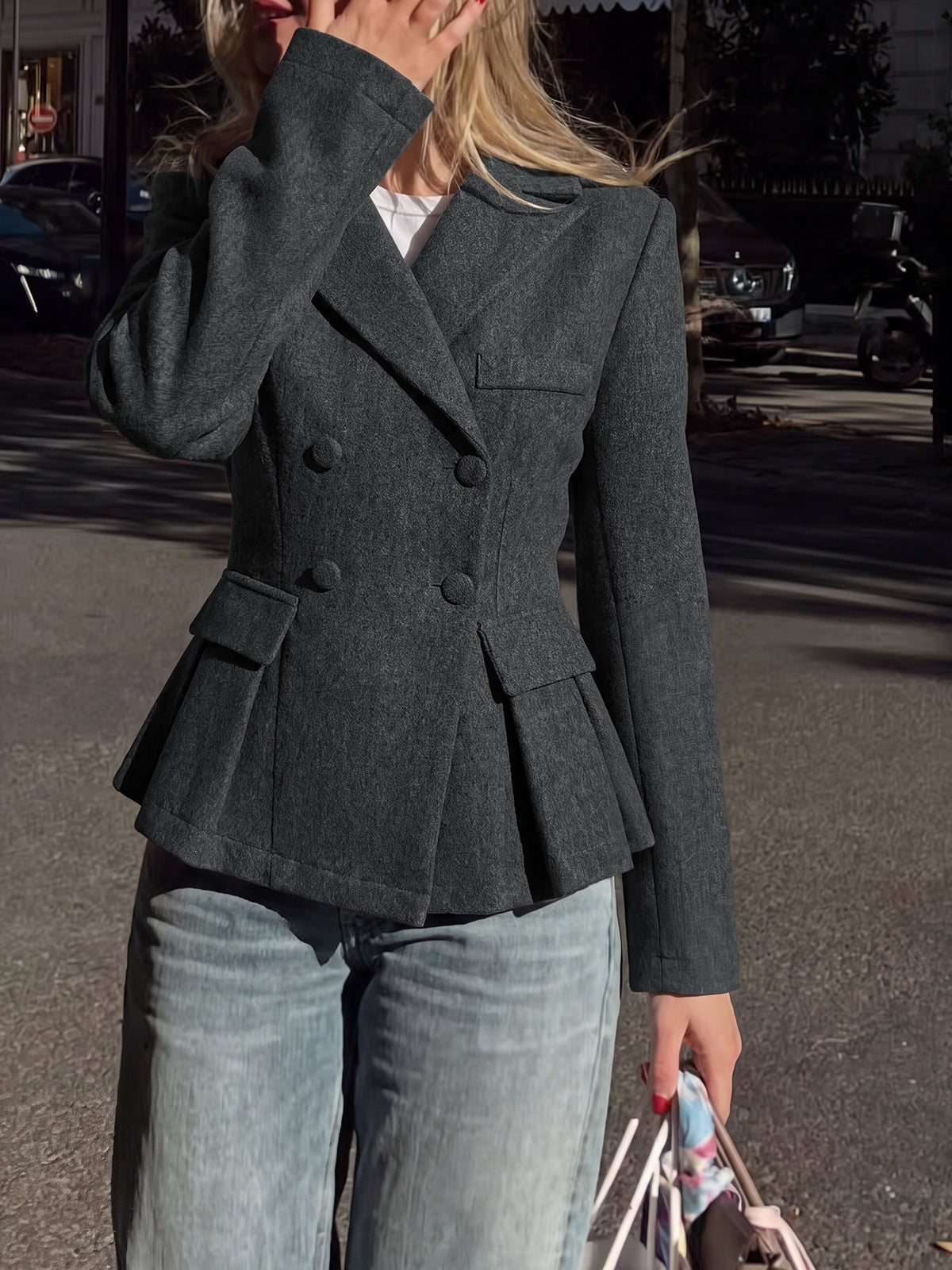 A woman wearing a dark gray double-breasted blazer with a peplum hem and light-wash blue jeans, standing outdoors on a street.