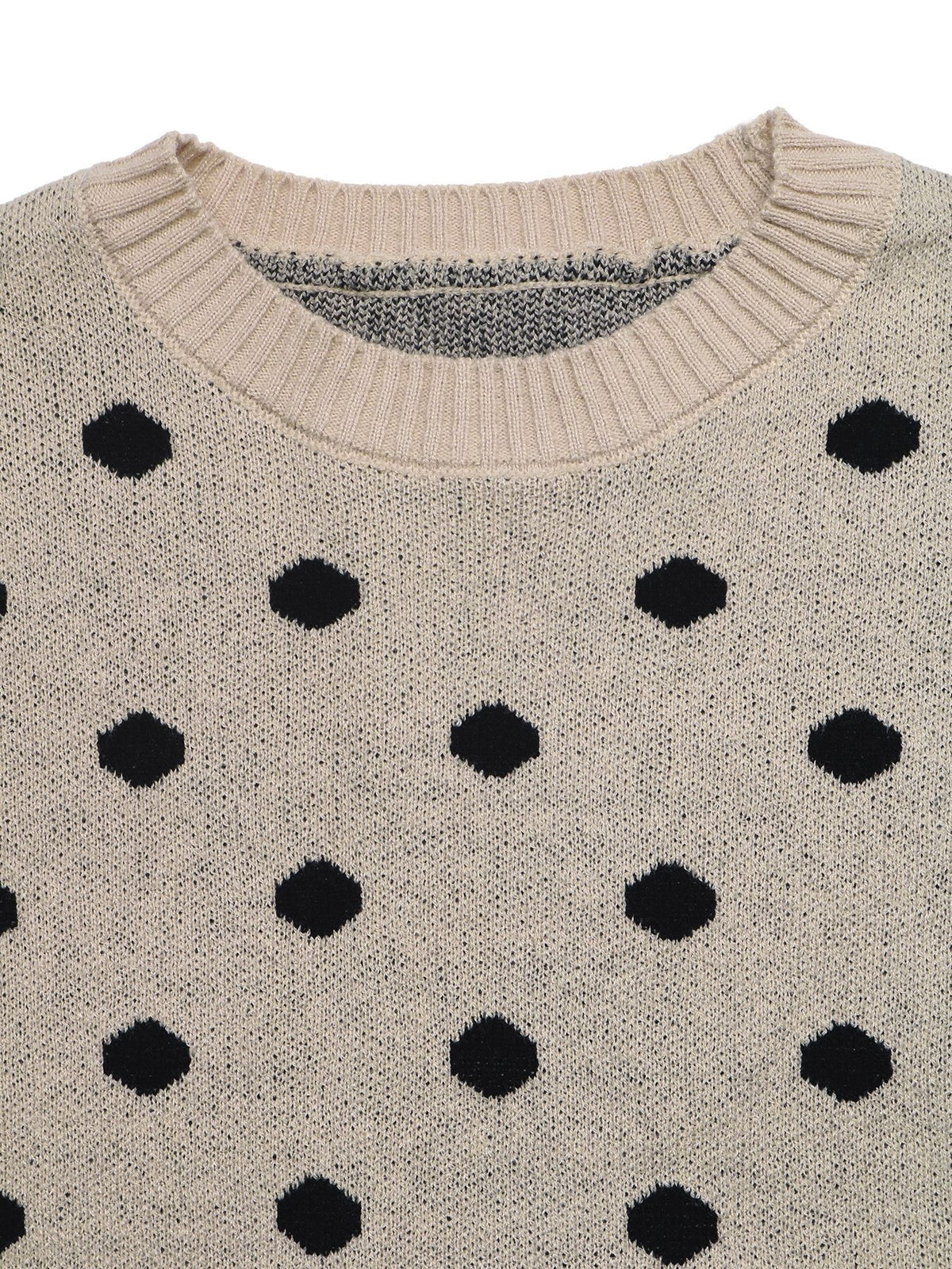 Close-up of a knit crewneck sweater in a warm beige or cream tone with a repeating black polka dot pattern.