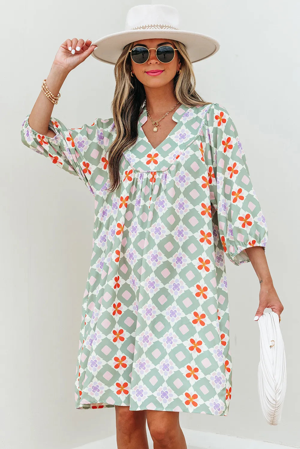 Woman wearing a floral dress with a white hat and sunglasses against a light background