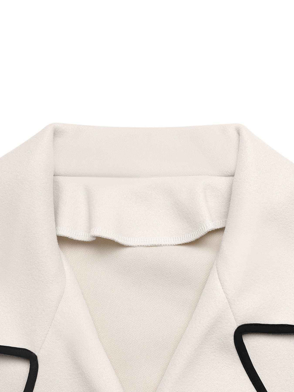 Close-up of a cream-colored jacket collar with black piping trim on a white background.