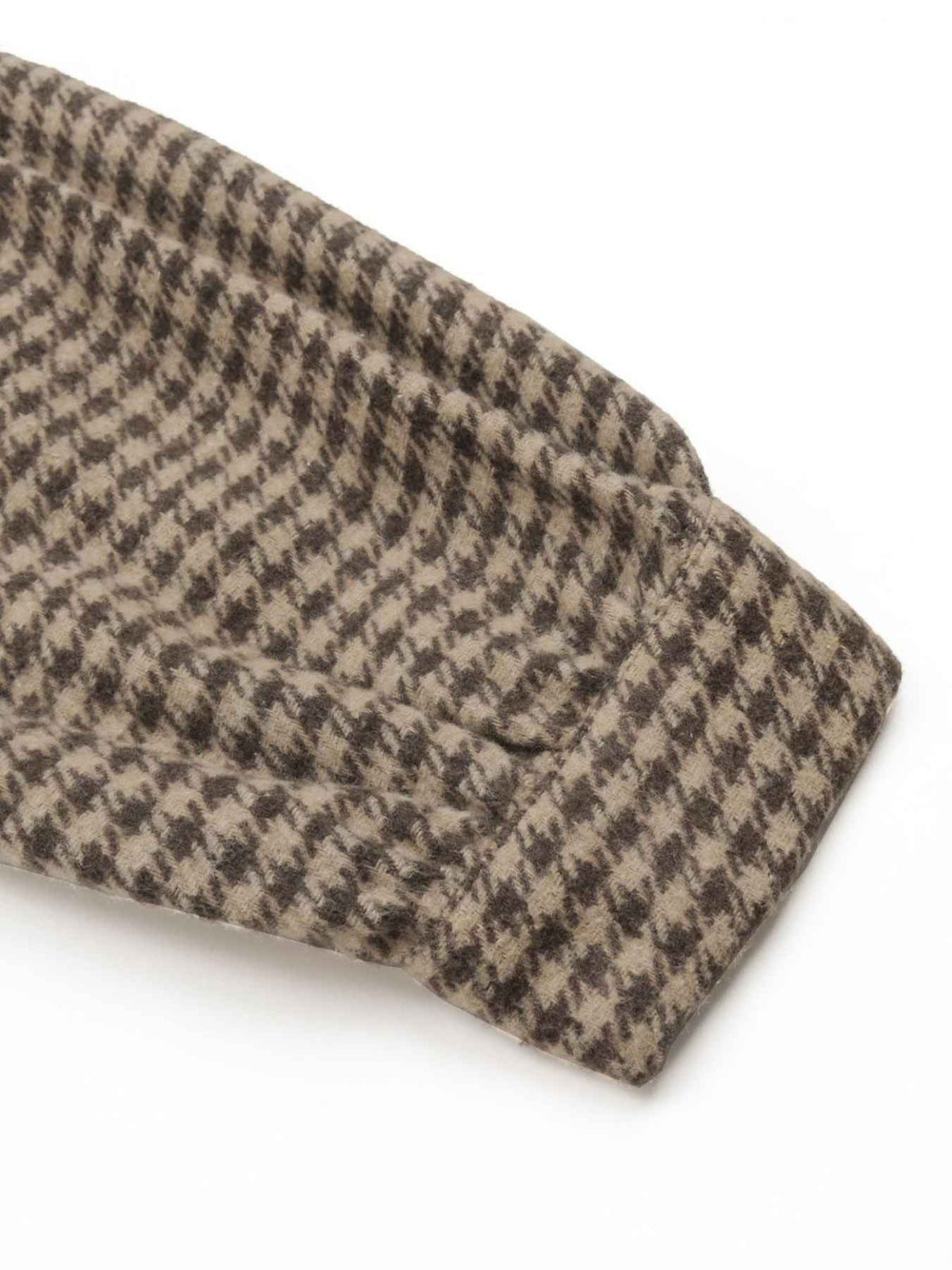 A close-up of a folded knit fabric with a brown and beige houndstooth pattern on a white background.