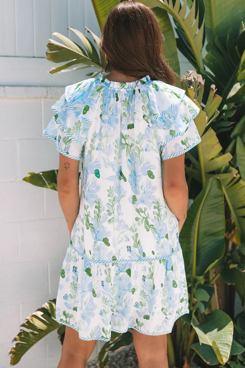 Person wearing a floral dress standing in front of tropical plants.