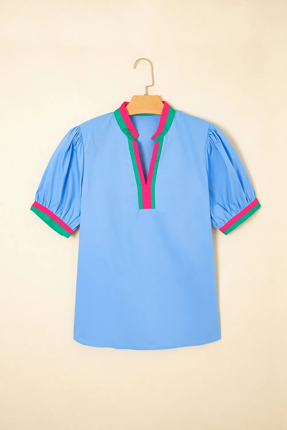 Blue blouse with colorful trim on a hanger against a beige background